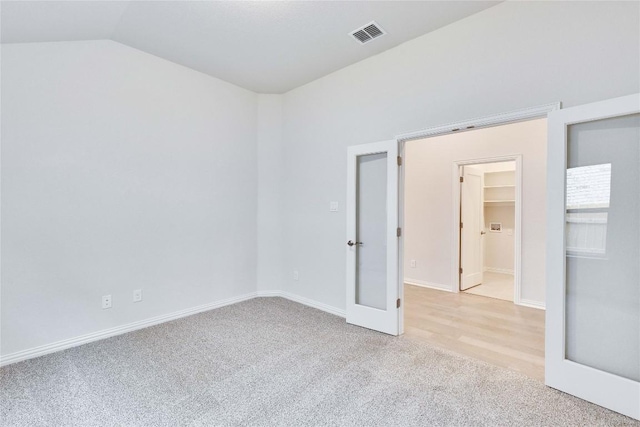 empty room featuring light colored carpet, visible vents, lofted ceiling, and baseboards