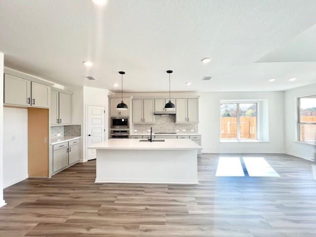 kitchen with hanging light fixtures, an island with sink, stainless steel appliances, and light hardwood / wood-style flooring