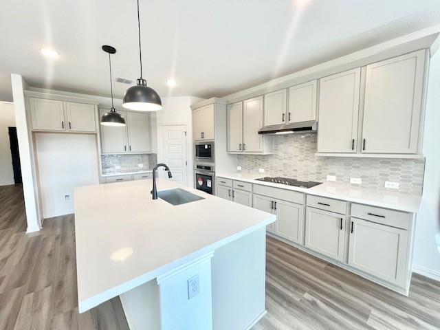 kitchen featuring backsplash, a center island with sink, hanging light fixtures, sink, and appliances with stainless steel finishes