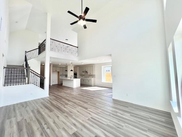 unfurnished living room with light wood-type flooring, high vaulted ceiling, and ceiling fan