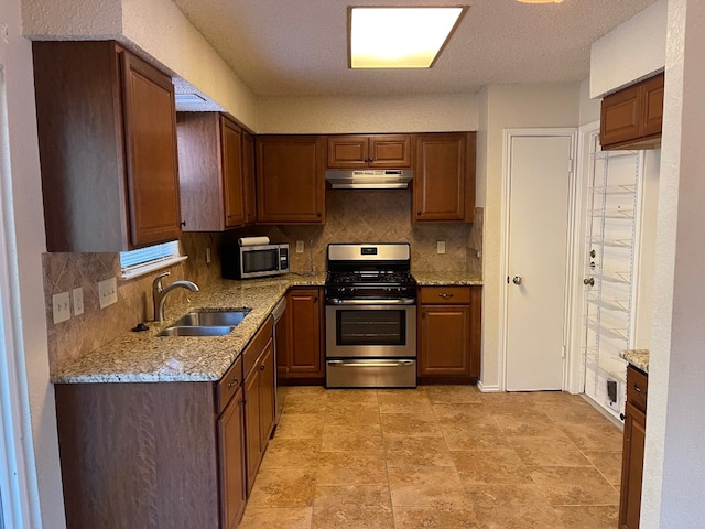 kitchen with decorative backsplash, appliances with stainless steel finishes, sink, and light stone counters