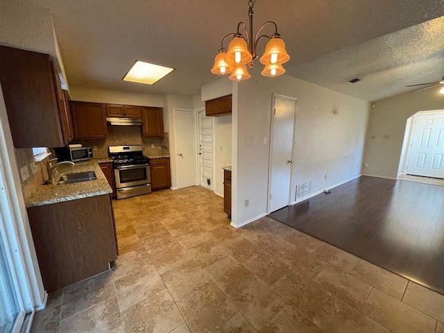 kitchen featuring tasteful backsplash, a textured ceiling, decorative light fixtures, appliances with stainless steel finishes, and light wood-type flooring