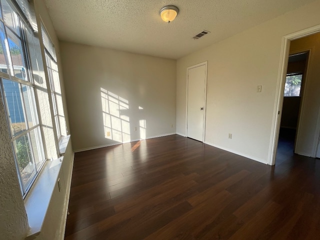 spare room featuring a textured ceiling, dark hardwood / wood-style flooring, and a wealth of natural light