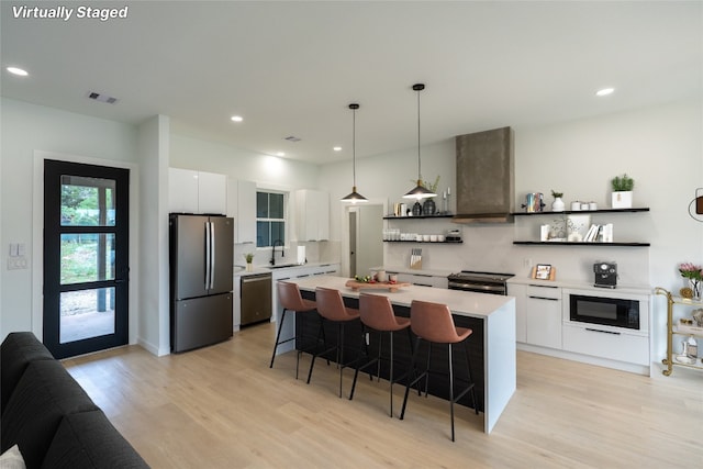 kitchen featuring white cabinets, sink, wall chimney range hood, stainless steel appliances, and a center island