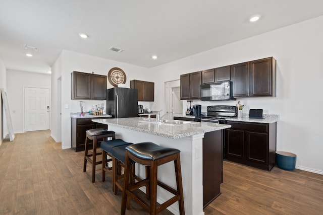 kitchen with a center island with sink, dark wood-type flooring, a kitchen breakfast bar, and black appliances