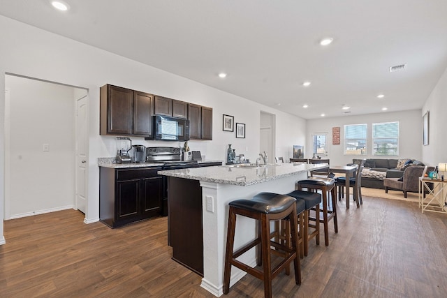 kitchen with a kitchen island with sink, a breakfast bar, dark wood-type flooring, sink, and dark brown cabinets