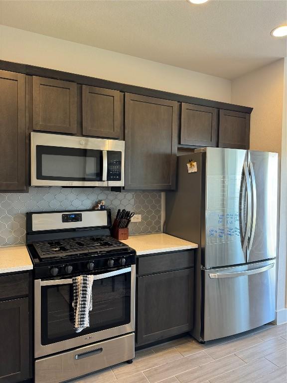 kitchen with appliances with stainless steel finishes, dark brown cabinets, tasteful backsplash, and light hardwood / wood-style flooring