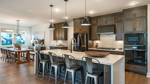 kitchen featuring an island with sink, decorative light fixtures, black appliances, and dark hardwood / wood-style floors