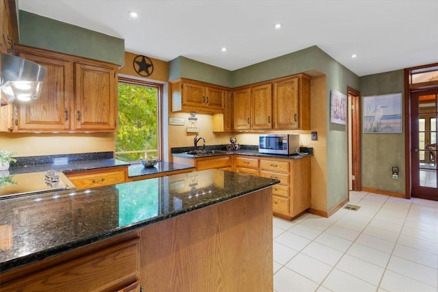 kitchen with light tile patterned flooring, stovetop, sink, dark stone countertops, and exhaust hood