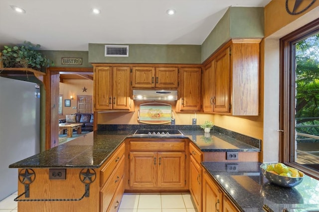 kitchen featuring cooktop, dark stone countertops, light tile patterned floors, and stainless steel fridge