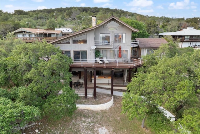 view of front of property with a view of trees, a deck, a patio area, and a chimney