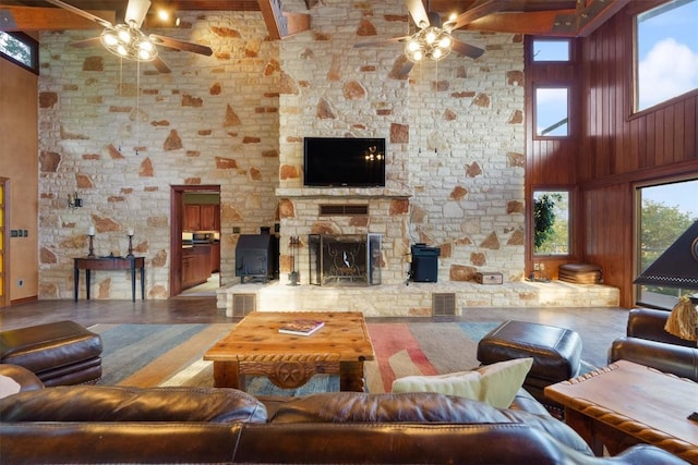 living room with a ceiling fan, a stone fireplace, and a high ceiling