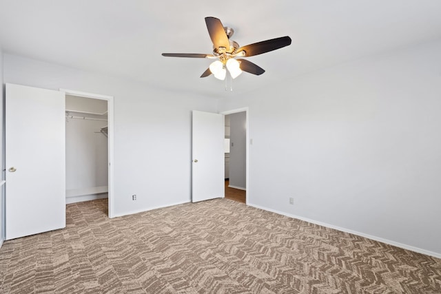 unfurnished bedroom with a spacious closet, a closet, carpet flooring, and ceiling fan