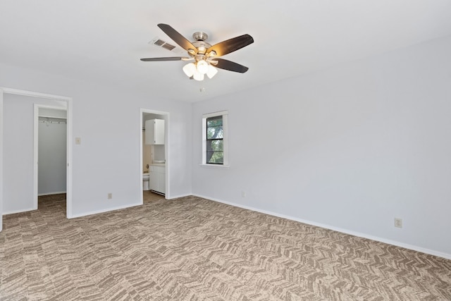 unfurnished bedroom with ceiling fan, a walk in closet, a closet, light colored carpet, and ensuite bath