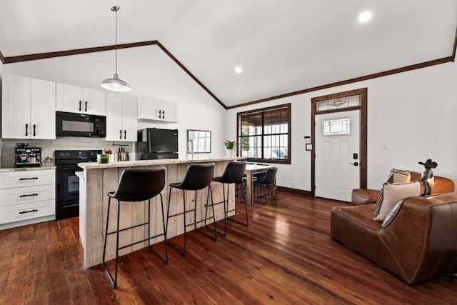 kitchen with pendant lighting, a center island with sink, dark wood-type flooring, white cabinetry, and black appliances