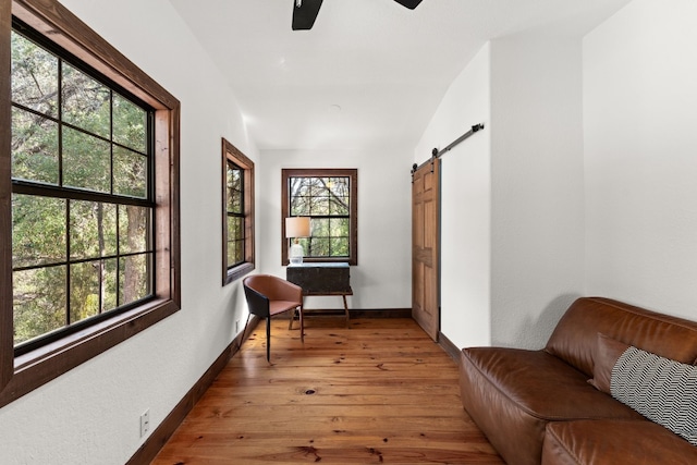 living area featuring wood-type flooring, a barn door, and ceiling fan