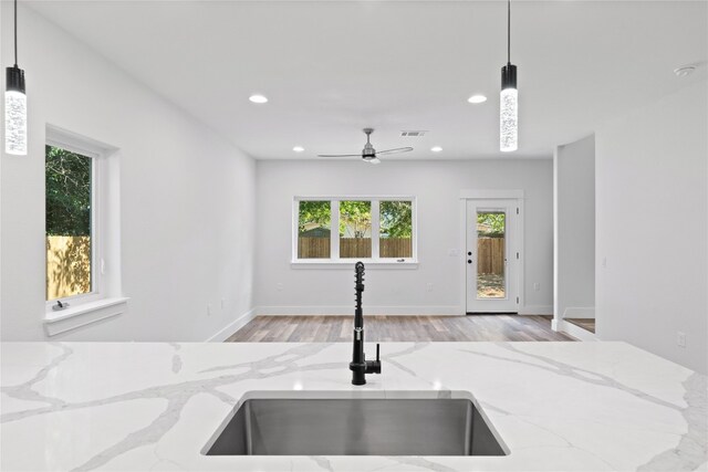 interior details featuring light wood-type flooring, light stone countertops, decorative light fixtures, and sink