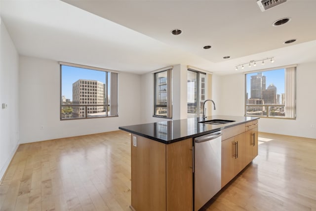 kitchen featuring dishwasher, a center island with sink, dark stone counters, and light hardwood / wood-style flooring