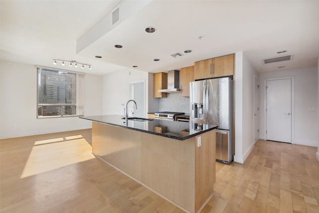 kitchen with wall chimney range hood, appliances with stainless steel finishes, sink, and an island with sink