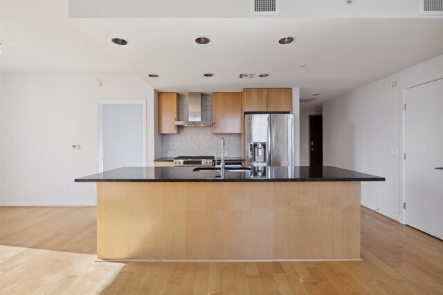 kitchen featuring wall chimney range hood, a kitchen island with sink, light hardwood / wood-style flooring, sink, and appliances with stainless steel finishes