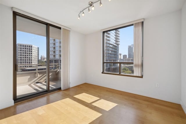 unfurnished room featuring a view of city, floor to ceiling windows, and wood finished floors