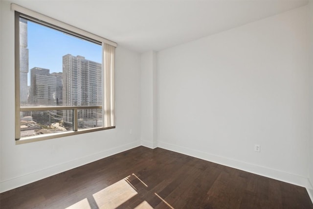 unfurnished room featuring baseboards, a view of city, and dark wood-type flooring