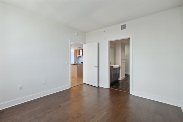 unfurnished bedroom featuring visible vents, baseboards, ensuite bathroom, and dark wood-style floors