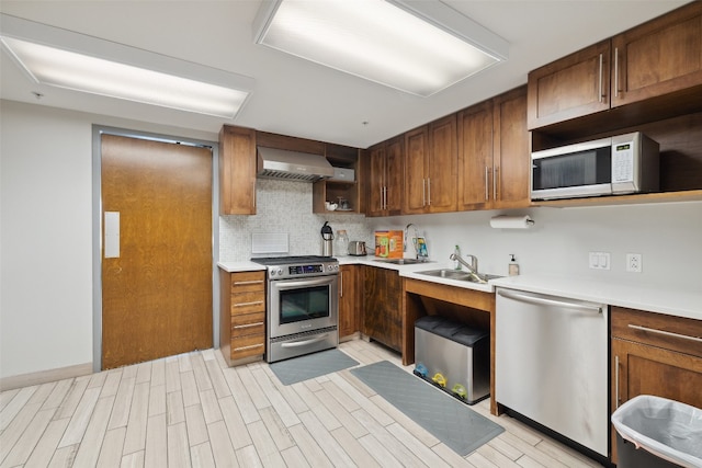 kitchen featuring tasteful backsplash, wall chimney range hood, appliances with stainless steel finishes, and sink