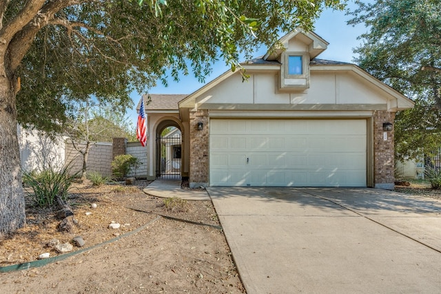 view of front of home featuring brick siding, a shingled roof, concrete driveway, an attached garage, and a gate