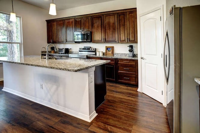 kitchen with light stone countertops, stainless steel appliances, dark wood-type flooring, sink, and decorative light fixtures