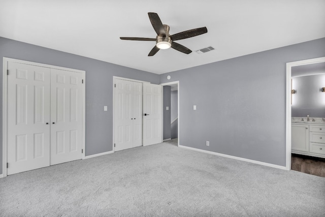 unfurnished bedroom with multiple closets, light carpet, ceiling fan, and ensuite bath