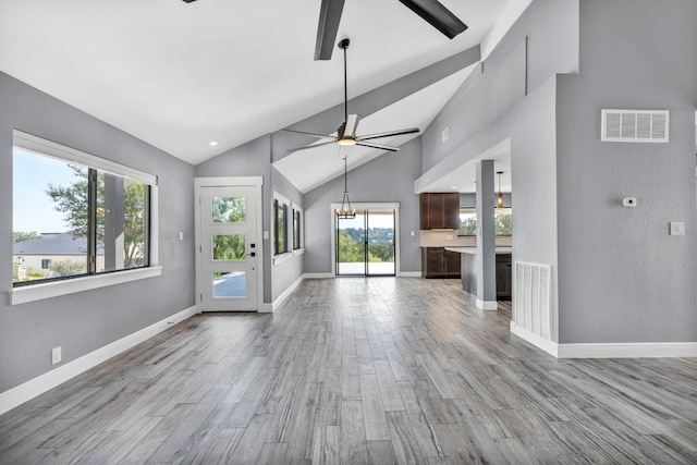 unfurnished living room with high vaulted ceiling, ceiling fan with notable chandelier, light wood-type flooring, and plenty of natural light