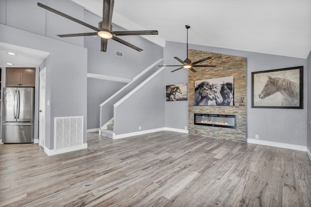 unfurnished living room featuring ceiling fan, light hardwood / wood-style floors, high vaulted ceiling, and a stone fireplace