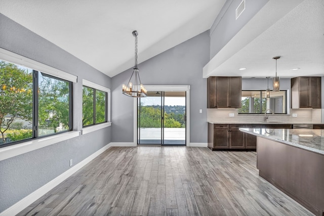 kitchen featuring dark brown cabinetry, light wood-type flooring, decorative light fixtures, an inviting chandelier, and light stone countertops