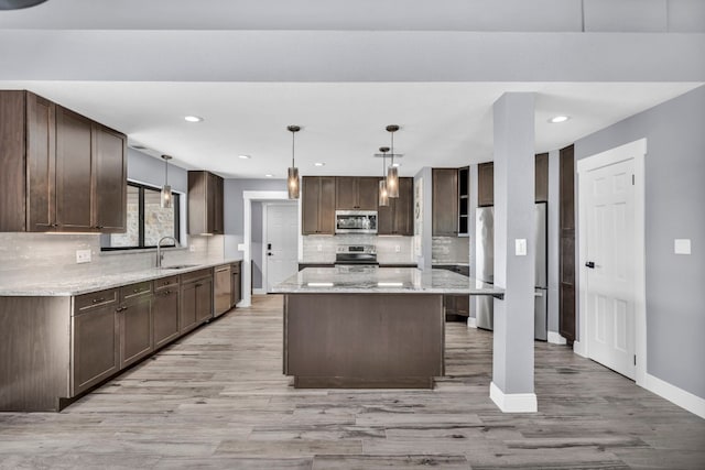 kitchen with pendant lighting, sink, stainless steel appliances, and light wood-type flooring