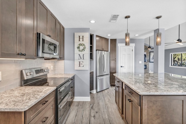 kitchen with light stone counters, ceiling fan, decorative light fixtures, appliances with stainless steel finishes, and light wood-type flooring