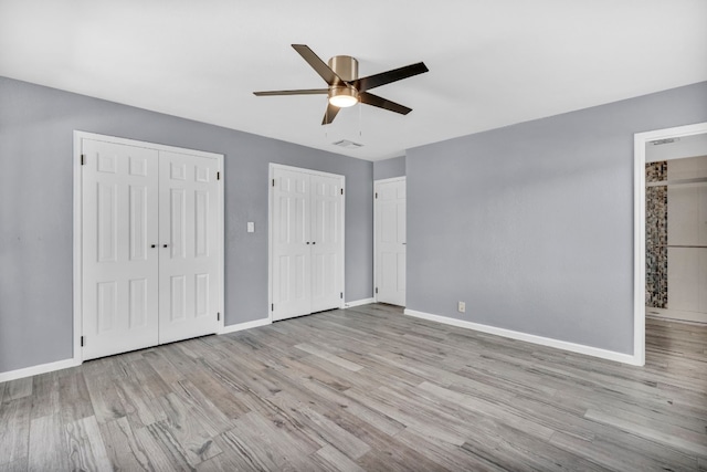 unfurnished bedroom featuring two closets, light hardwood / wood-style floors, and ceiling fan