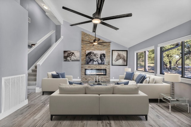 living room with a stone fireplace, high vaulted ceiling, light wood-type flooring, and ceiling fan