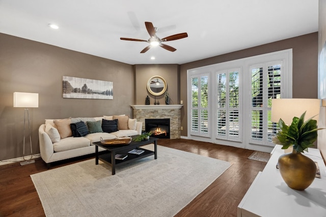 living room featuring ceiling fan, dark hardwood / wood-style floors, and a stone fireplace