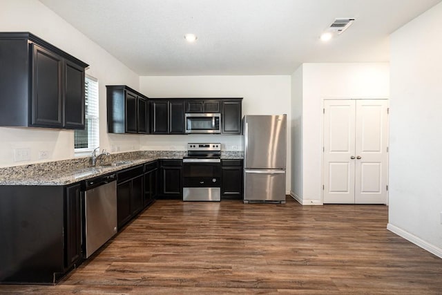 kitchen with light stone counters, visible vents, appliances with stainless steel finishes, a sink, and dark cabinetry