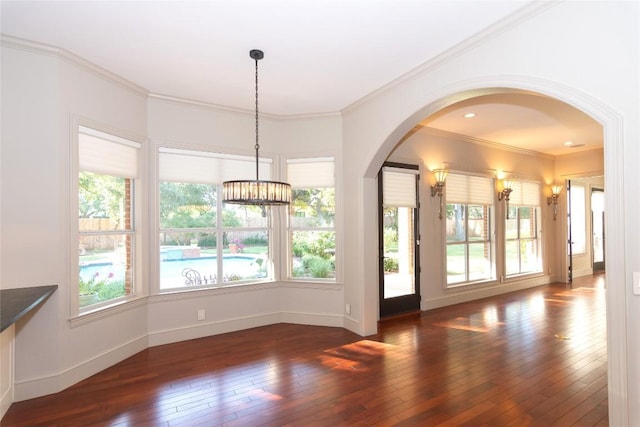 unfurnished dining area featuring crown molding, hardwood / wood-style flooring, arched walkways, an inviting chandelier, and baseboards