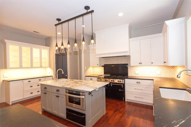 kitchen featuring pendant lighting, dark wood-type flooring, sink, an island with sink, and white cabinetry