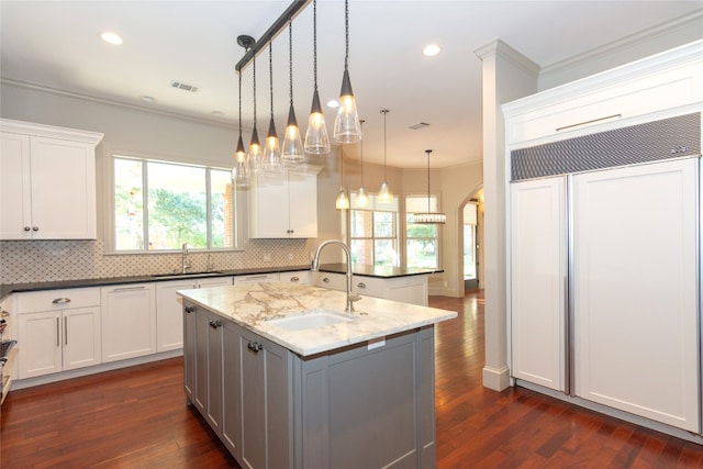 kitchen with a kitchen island with sink, dark wood-type flooring, sink, pendant lighting, and dark stone counters