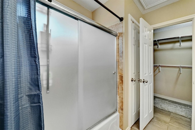 full bath with a walk in closet, baseboards, bath / shower combo with glass door, and a textured ceiling