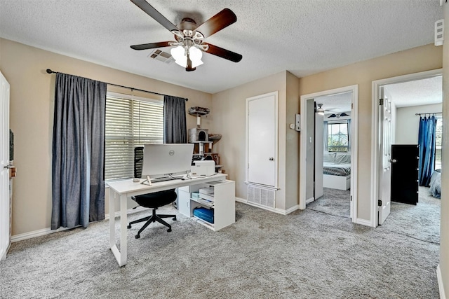 carpeted office with visible vents, plenty of natural light, a textured ceiling, and a ceiling fan