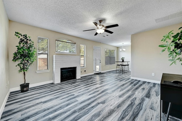 unfurnished living room with baseboards, wood finished floors, a fireplace, and ceiling fan with notable chandelier