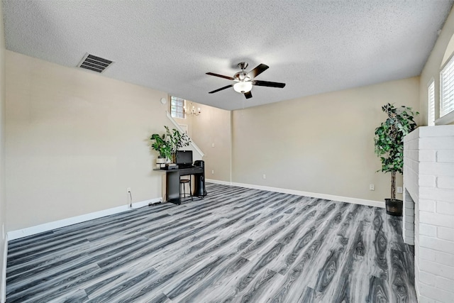 unfurnished living room featuring a ceiling fan, wood finished floors, visible vents, baseboards, and a textured ceiling