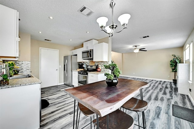 dining area with visible vents, light wood-style floors, and ceiling fan with notable chandelier