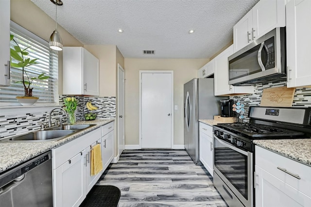 kitchen with visible vents, a sink, wood finished floors, stainless steel appliances, and white cabinets