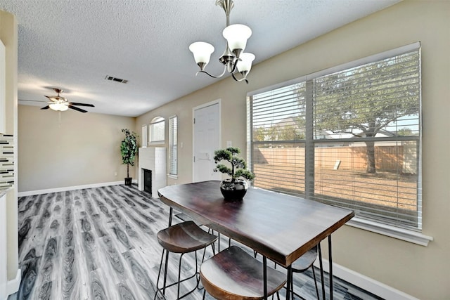 dining space featuring baseboards, a fireplace, light wood-type flooring, and a textured ceiling